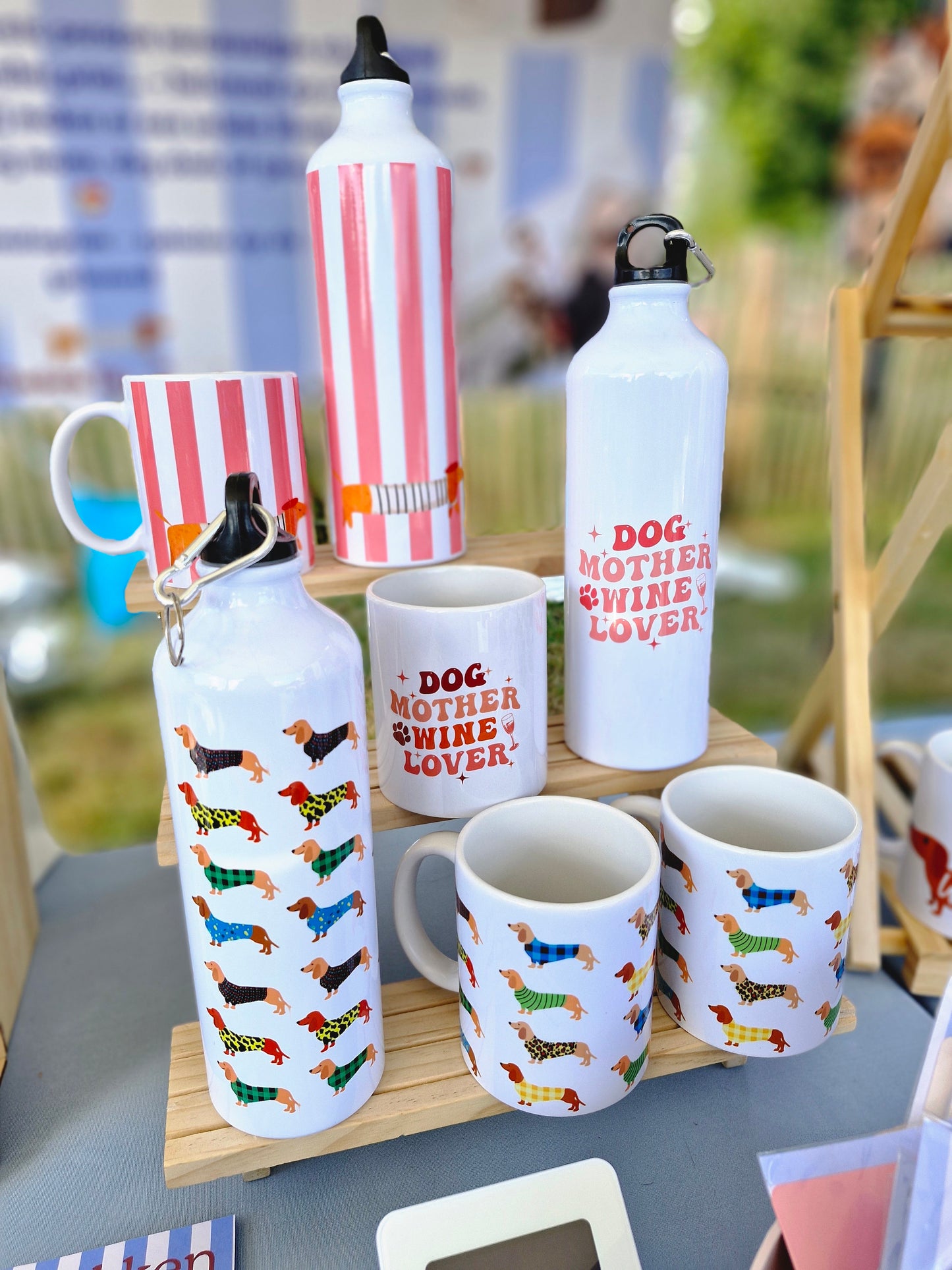 beeld van op een dog markt met waterflessen en mokken waar er een reeks van is: verschillende teckels, dog mother wine lover en de la saucisse parisienne zalmroze strepen met een teckel parijse stijl