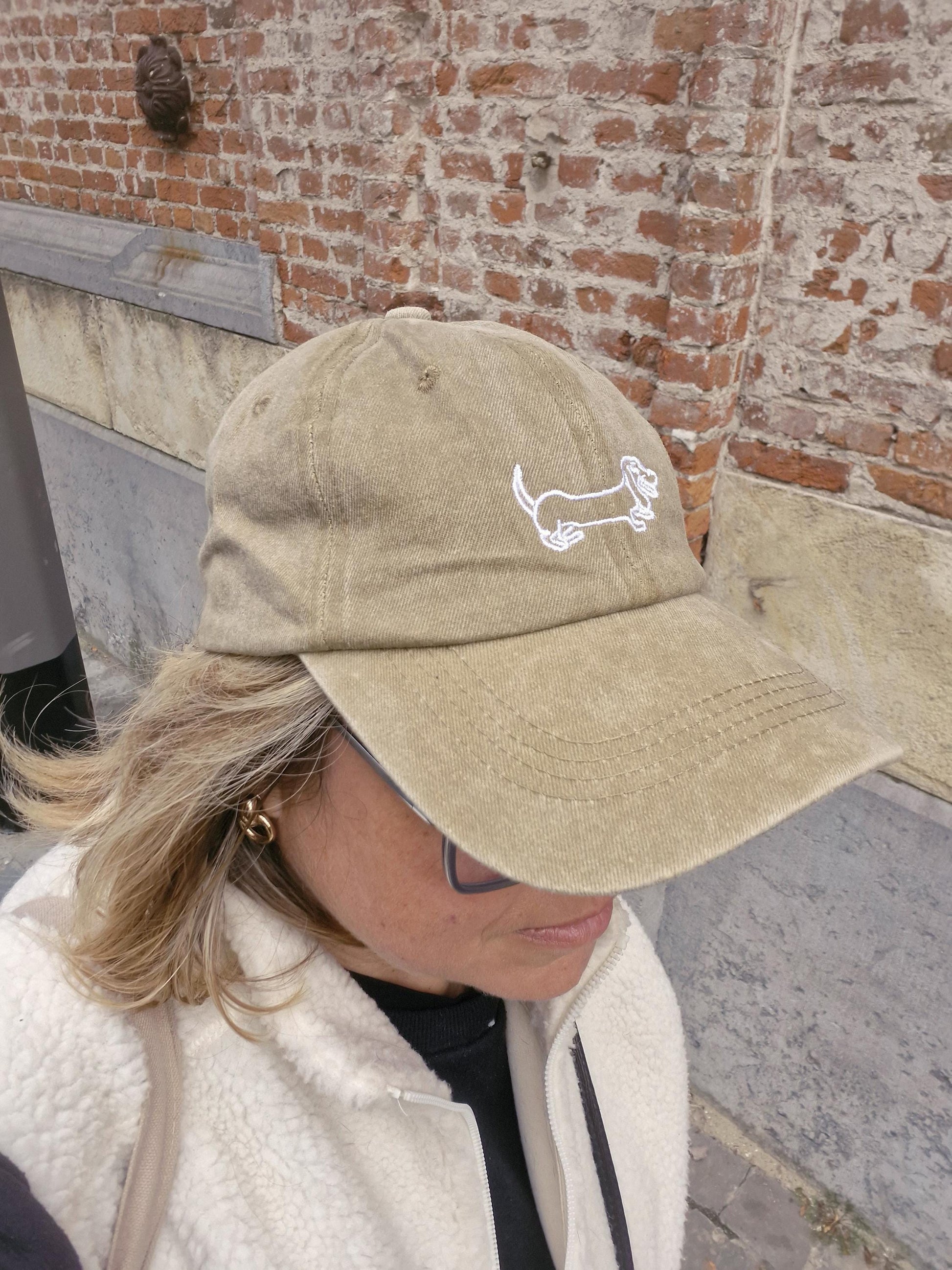 Dame die met een beige pet met geborduurde teckel loopt