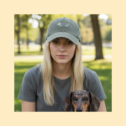 vrouw met kaki petje waar een teckel op geborduurd staat, er zit een merle teckel bij haar