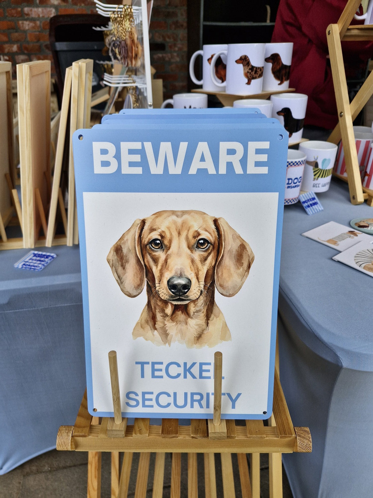 Waakbord teckel korthaar rood - Beware Teckel Security bordje in het blauw op de marktkraam van Teckels Tales Travels