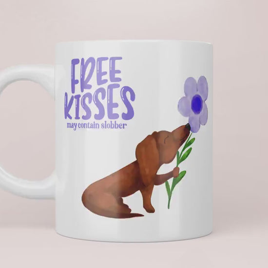 Video Mok met lila tekst “free kisses may contain slobber” met een bruine teckel op die een lila bloem vast heeft