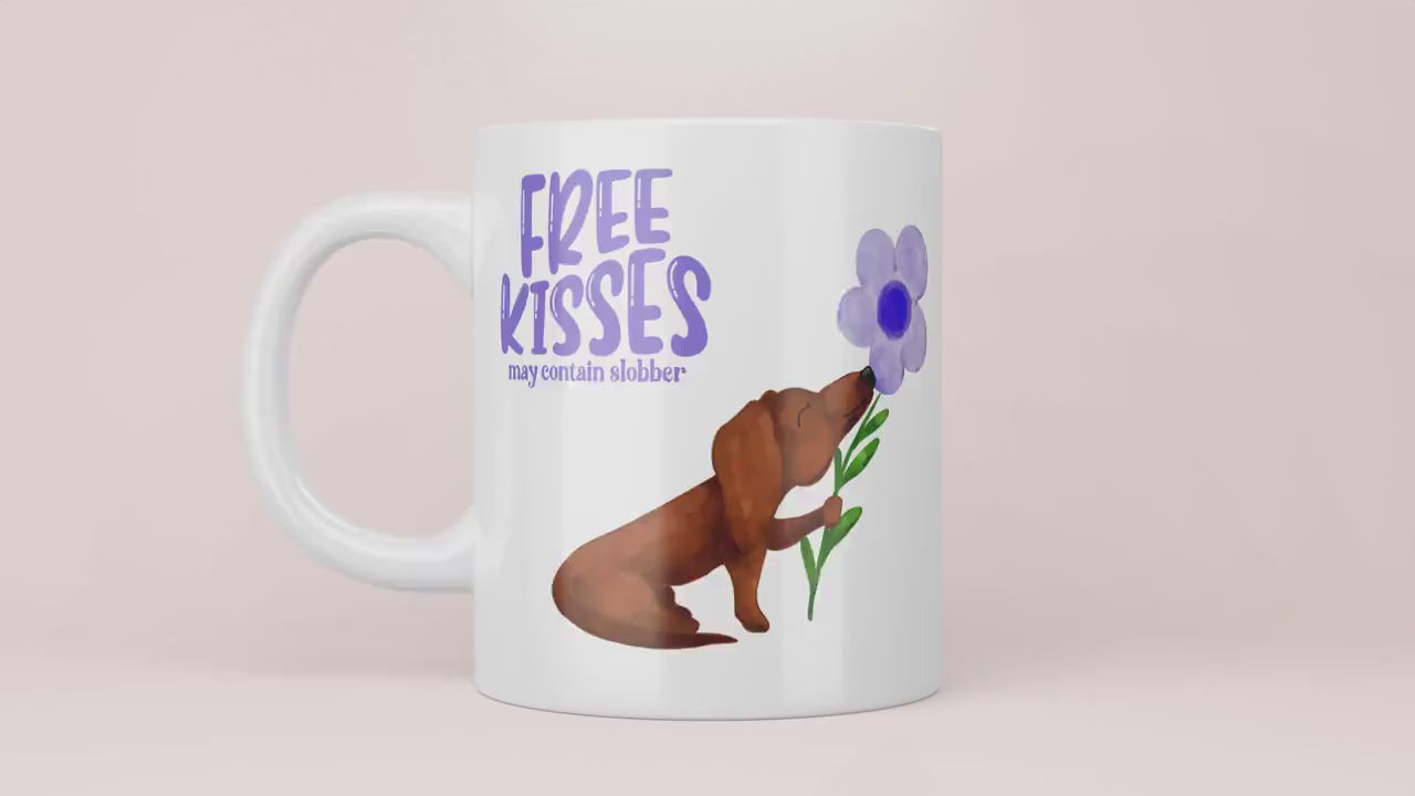 Video Mok met lila tekst “free kisses may contain slobber” met een bruine teckel op die een lila bloem vast heeft