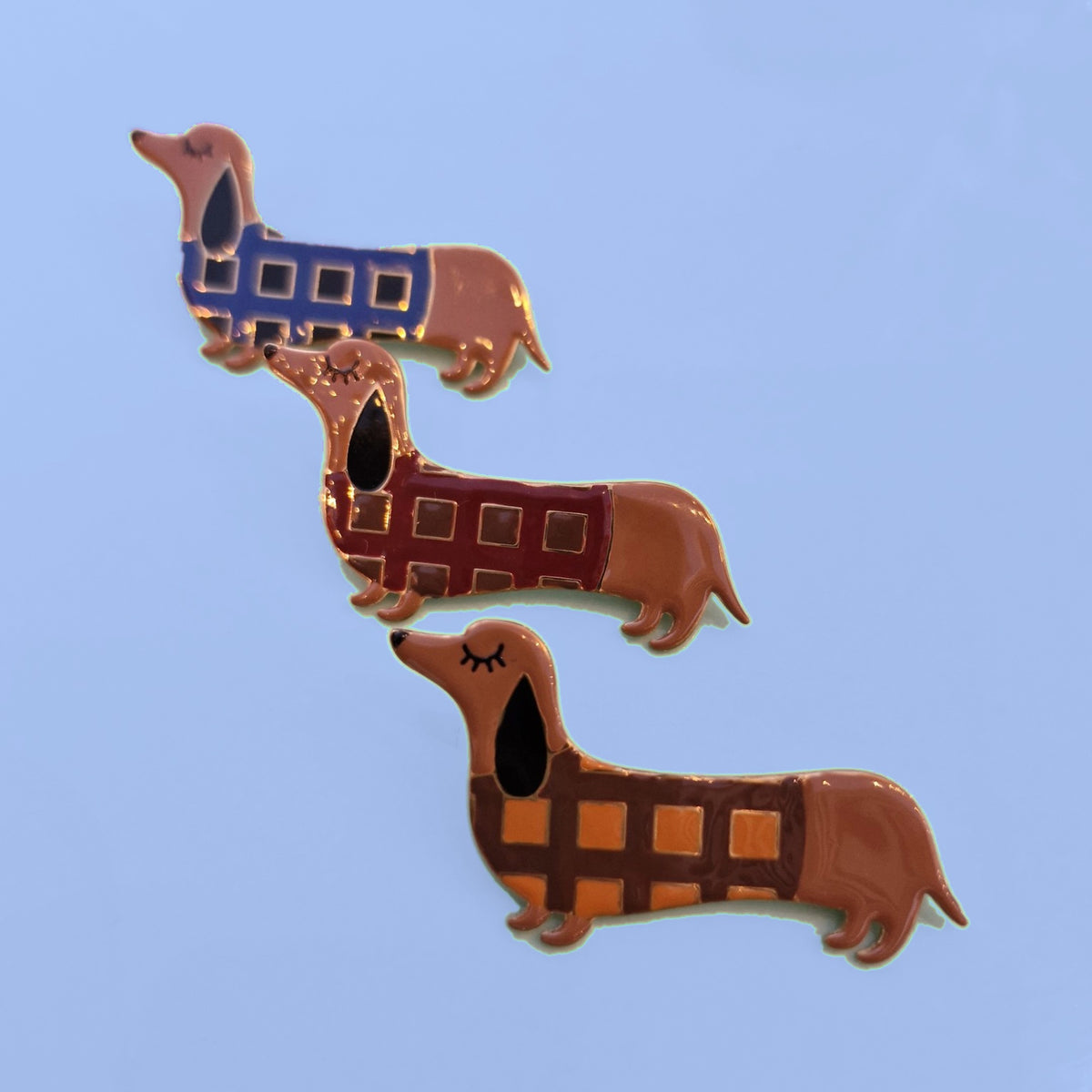 Drie teckel broches met geruite truitjes in blauw, bordeaux en bruin-oker