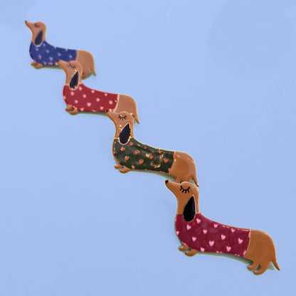 Vier teckel broches met hartjestruitjes in blauw, rood, groen en fuchsia op lichtblauwe achtergrond