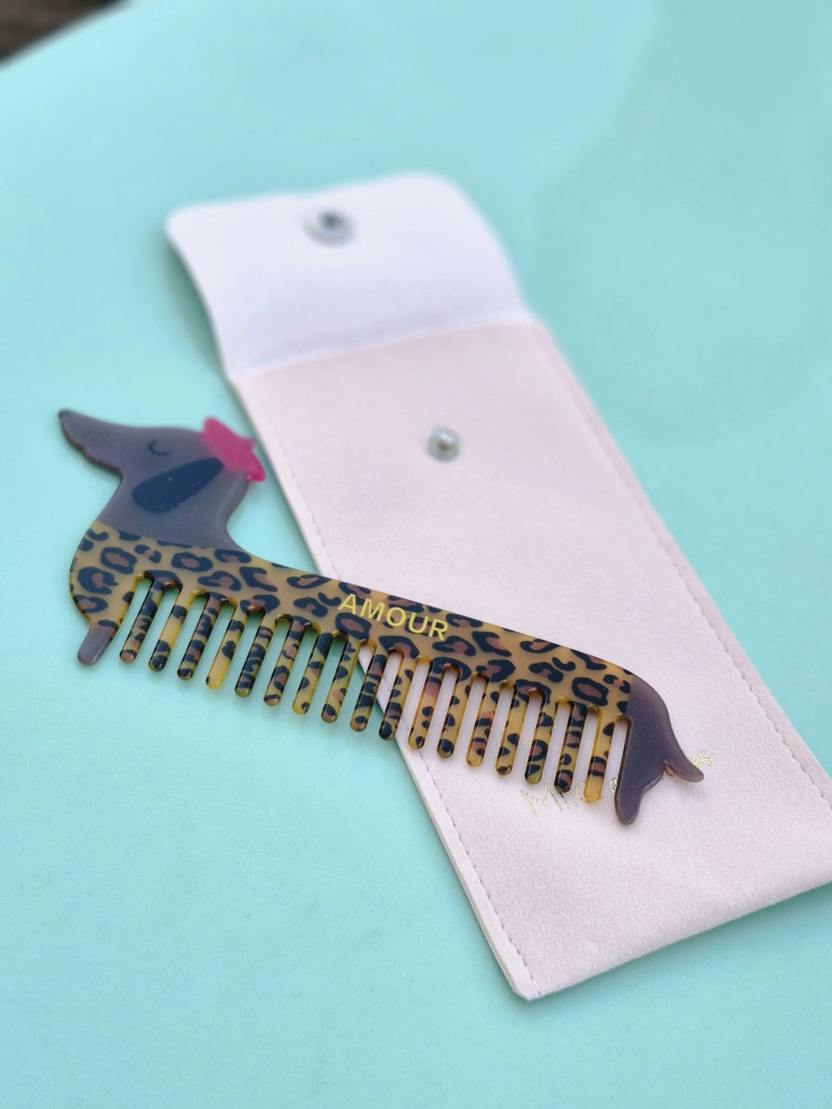 Luipaardprint teckelkam naast het roze fluwelen hoesje met drukknoop