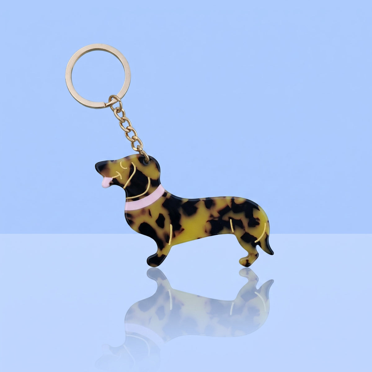 Teckel sleutelhanger schildpadprint met roze halsband en goudkleurige ring op lichtblauwe achtergrond
